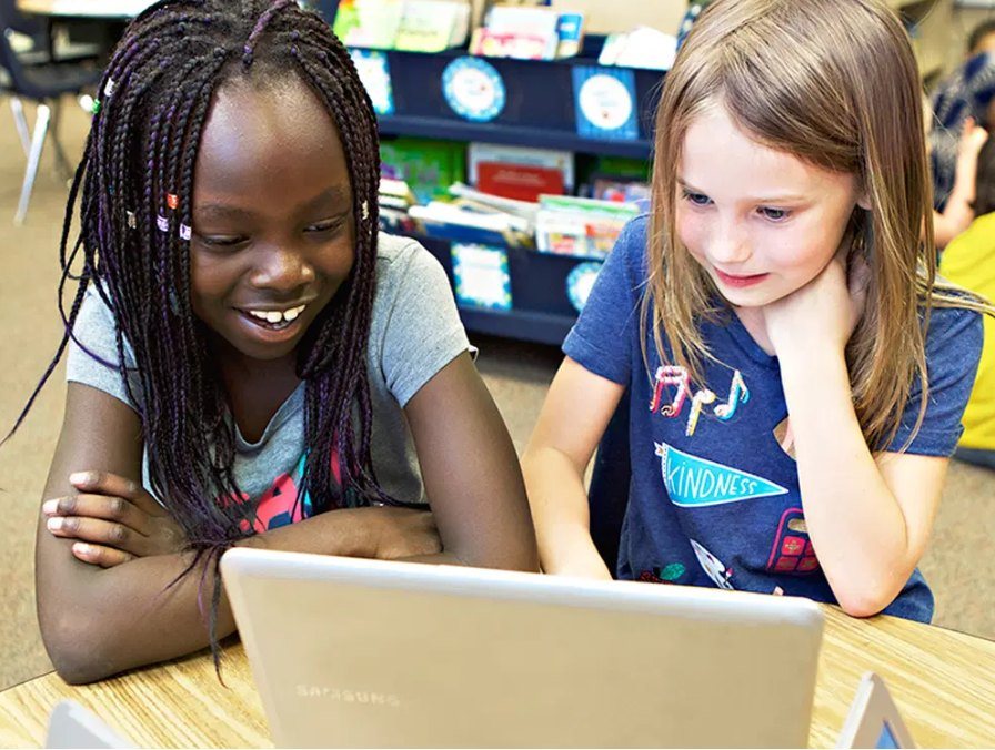 Two students smiling at a laptop together in a classroom